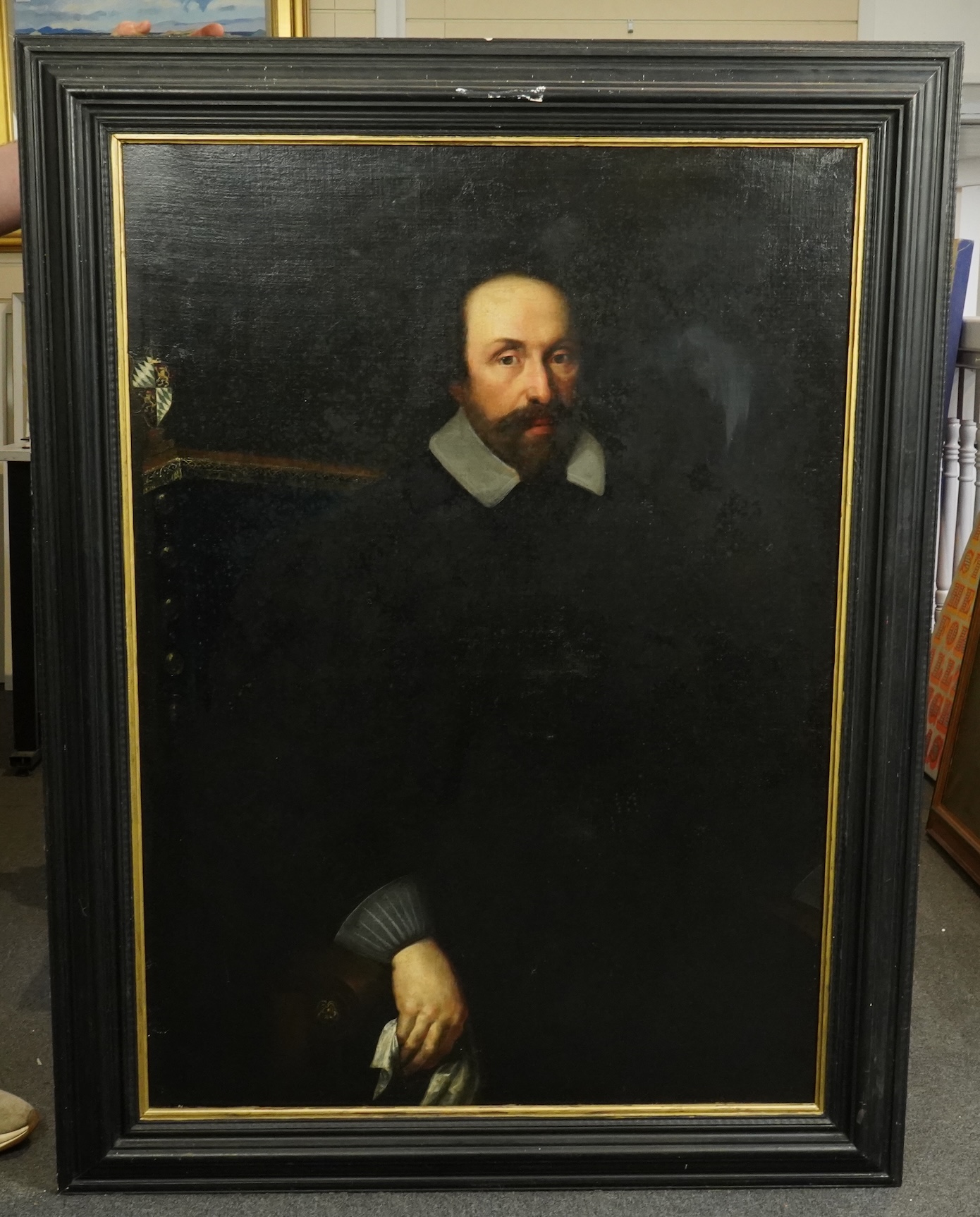 17th century Dutch School , Half length portrait of a seated gentleman, an armorial beyond, oil on canvas, 113 x 81cm